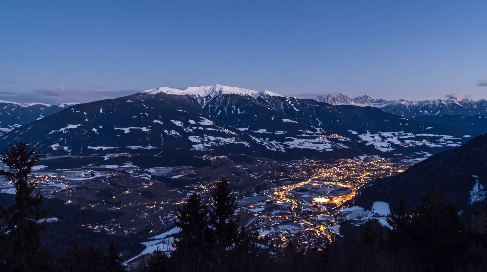 Abendstimmung über einem beleuchteten Tal mit verschneiten Bergen