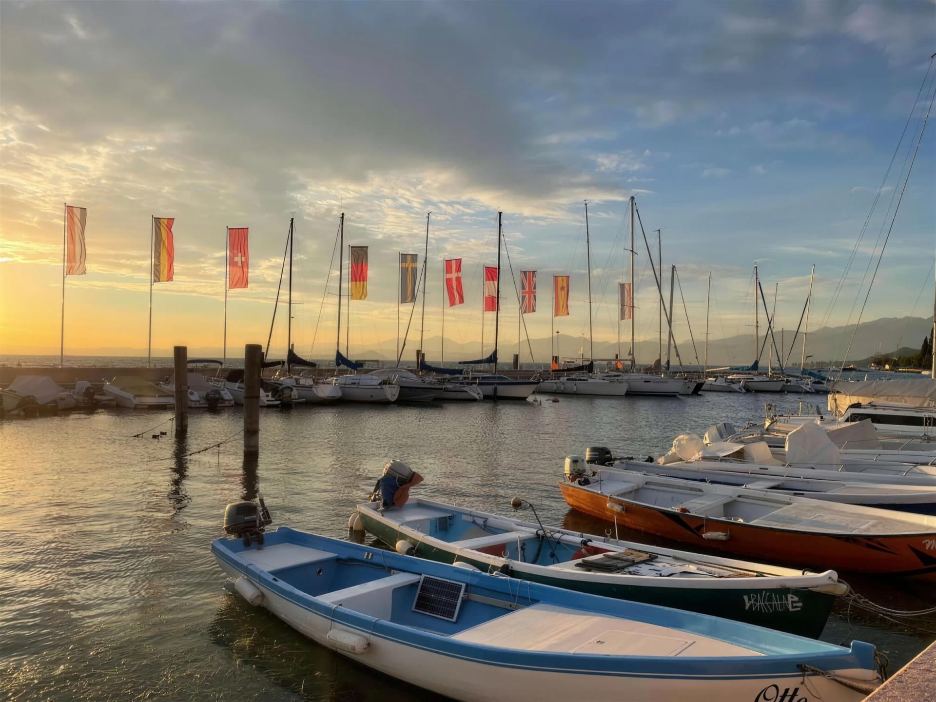 Small harbour with rowing boats, sailing boats and flags at sunset